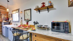 Una cocina con una isla central, taburetes de bar, horno tostador y diversos utensilios de cocina.