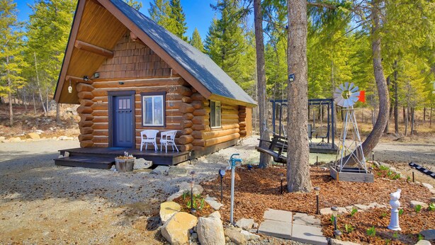 Una cabaña de troncos con un porche, mobiliario exterior y un molino.