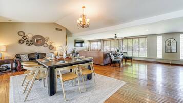 A spacious living room with a dining area, wooden flooring, and a large chandelier.
