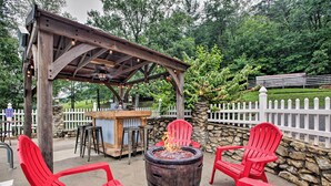 Una pérgola de madera con un hogar a leña y sillas Adirondack rojas.