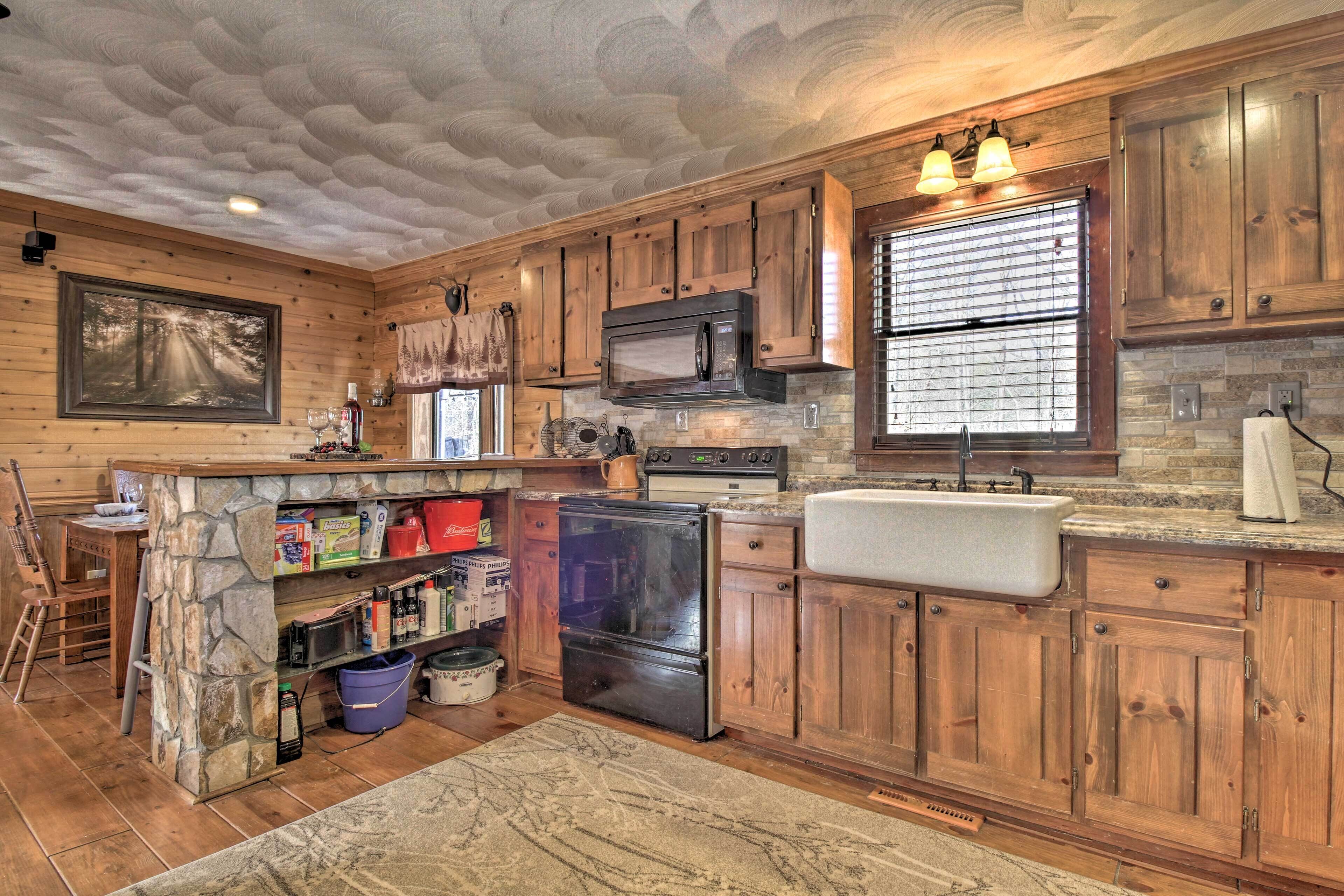 A rustic kitchen with wooden cabinets, a stone island, and a large window.