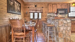 Interior de una cabaña de madera con una mesa de comedor, sillas, una barra de piedra y una zona de cocina.