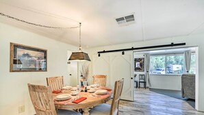 A dining area with a wooden table set for six, surrounded by chairs. A large window provides natural light, and a sliding barn door leads to another room. - Sedona Stardust Hideaway' w/ Patio & Mtn Views! (Sedona)