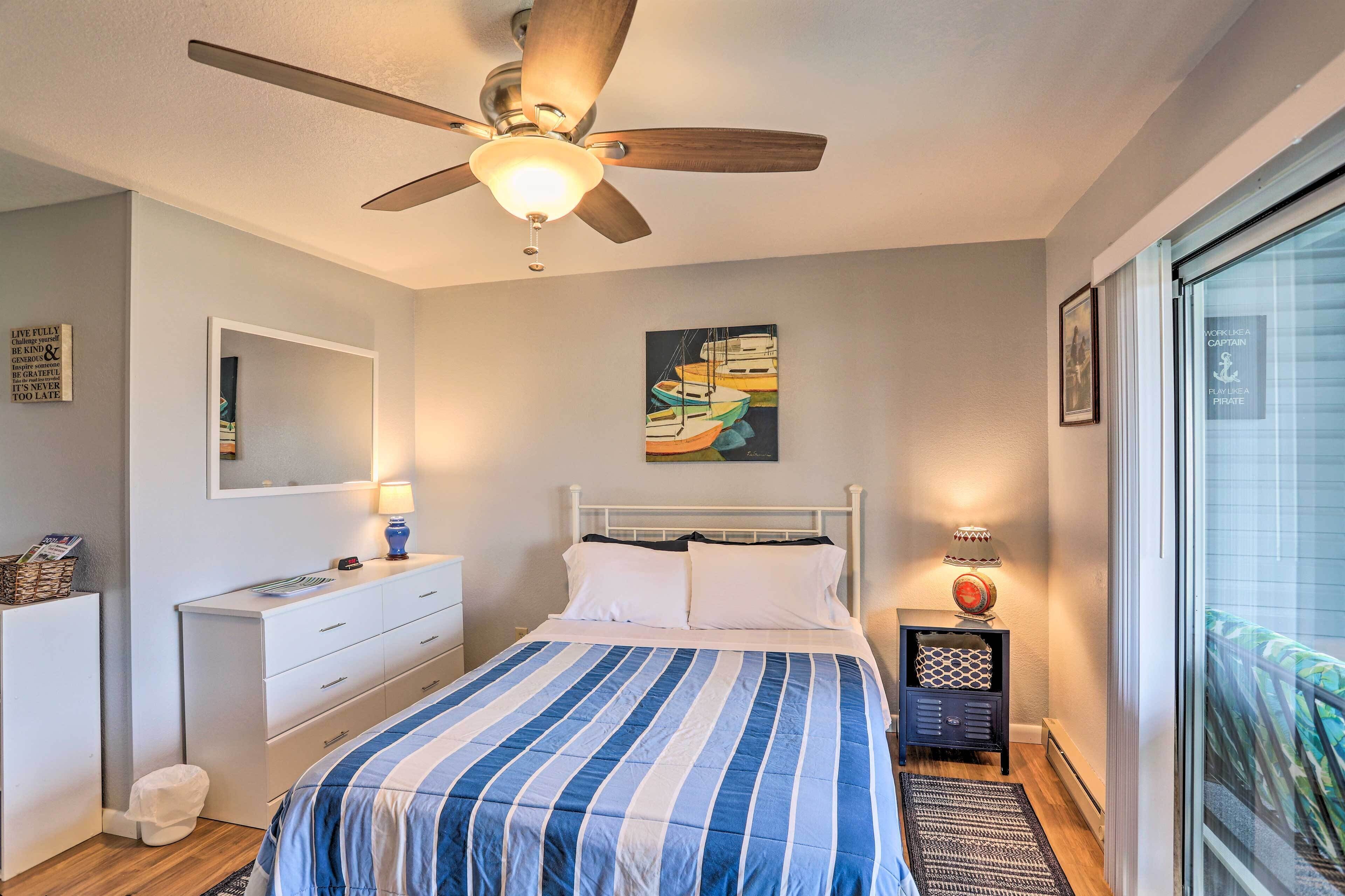 Une chambre à coucher comprenant un lit, un ventilateur de plafond, une table de chevet, une commode, un miroir et une fenêtre donnant sur un paysage agréable.