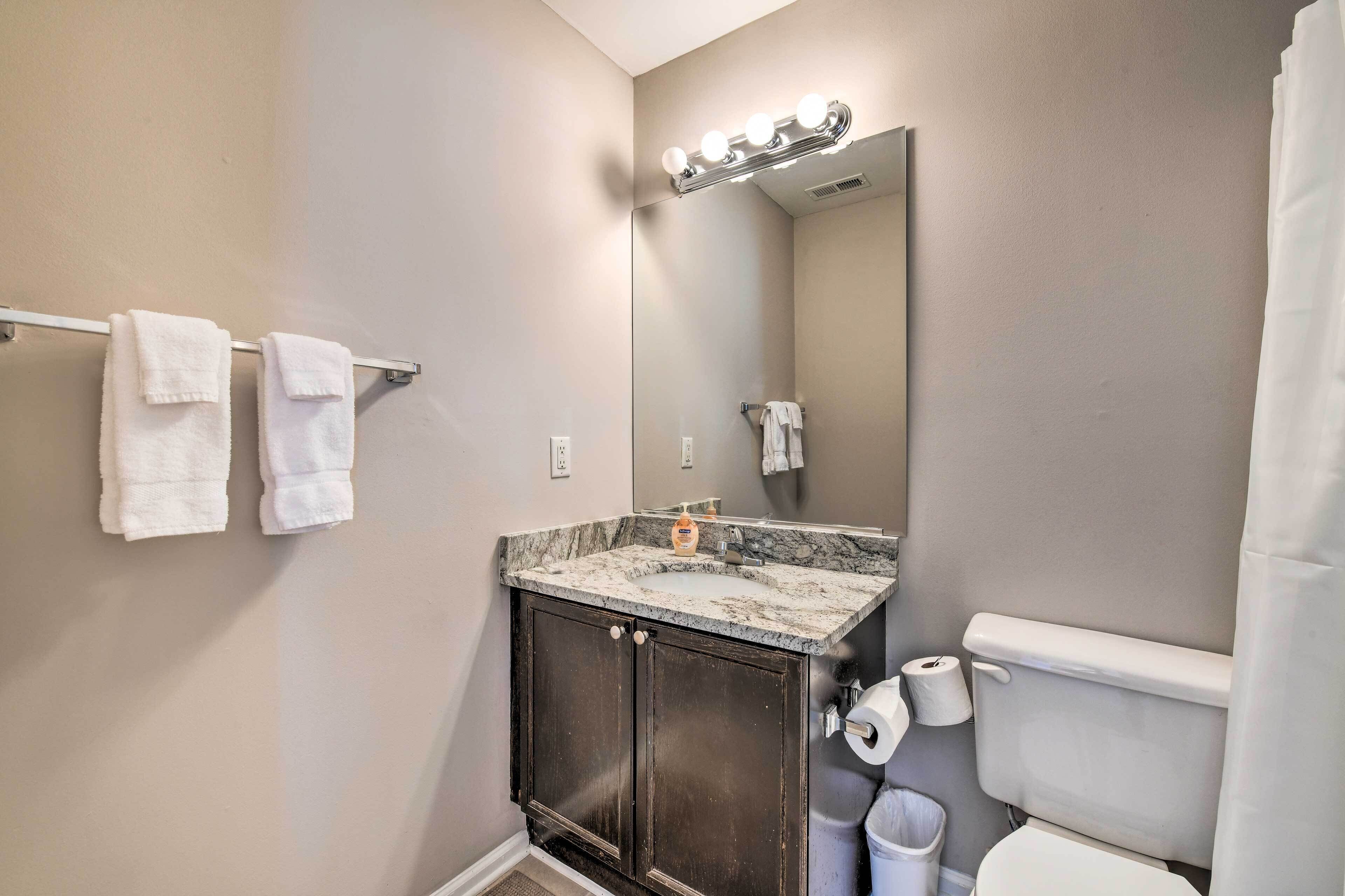 A bathroom with a marble sink, dark cabinets, a mirror with lights, a toilet, and a towel rack.
