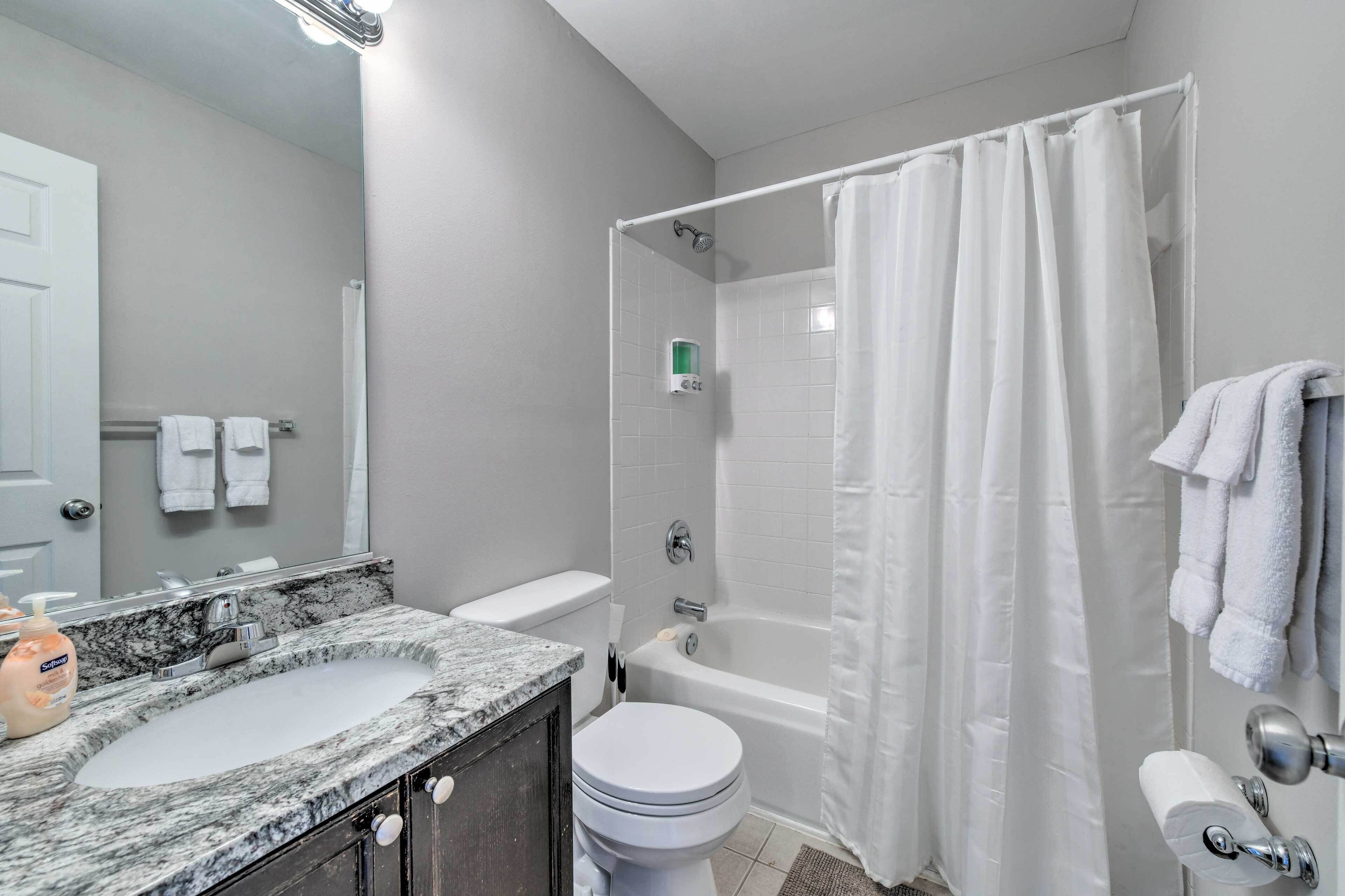 A bathroom with a marble sink, white toilet, bathtub, and a shower curtain.