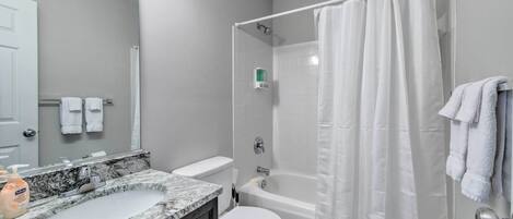 A bathroom with a marble sink, white toilet, bathtub, and a shower curtain.