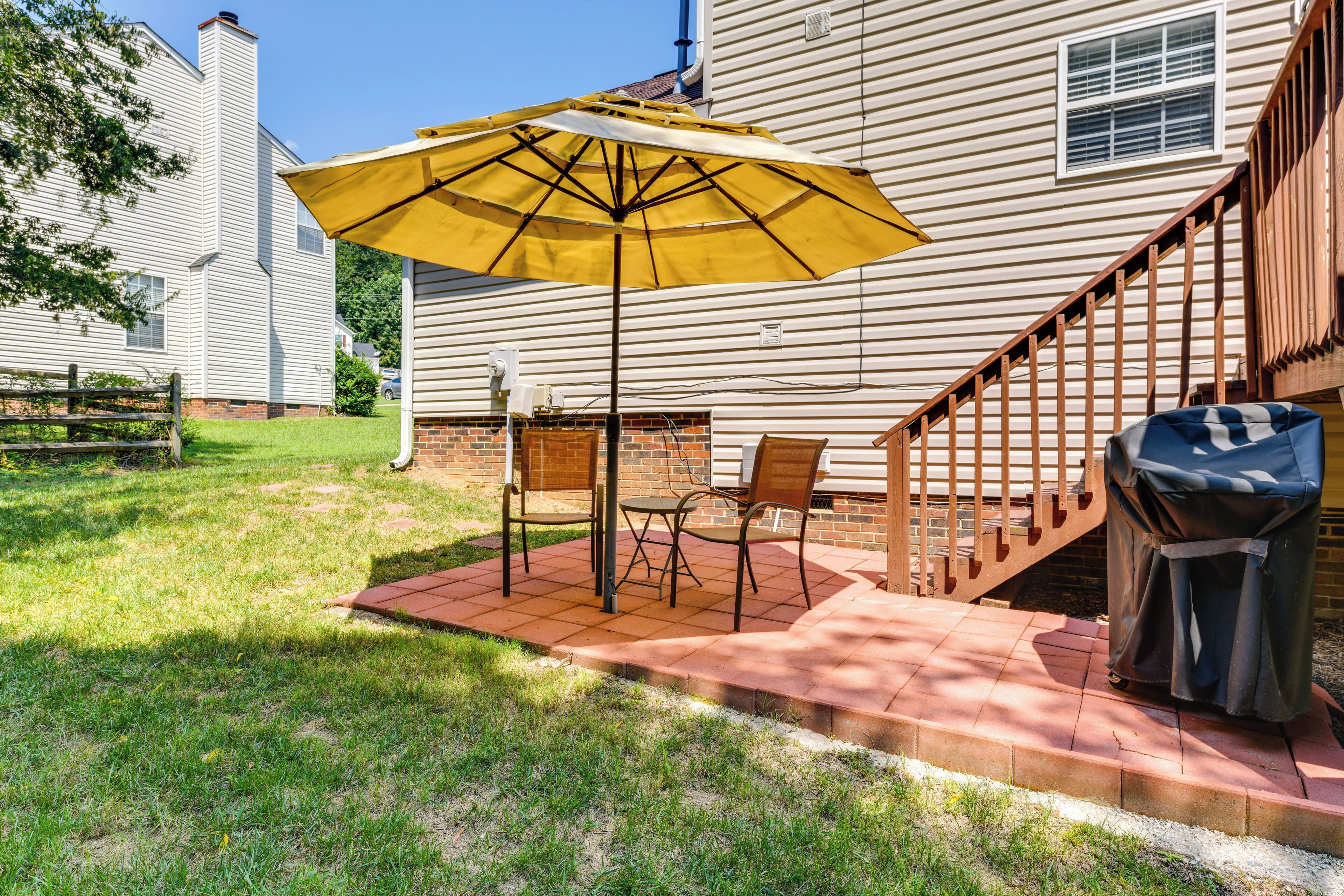 A patio with a yellow umbrella, outdoor furniture, and a barbecue grill.