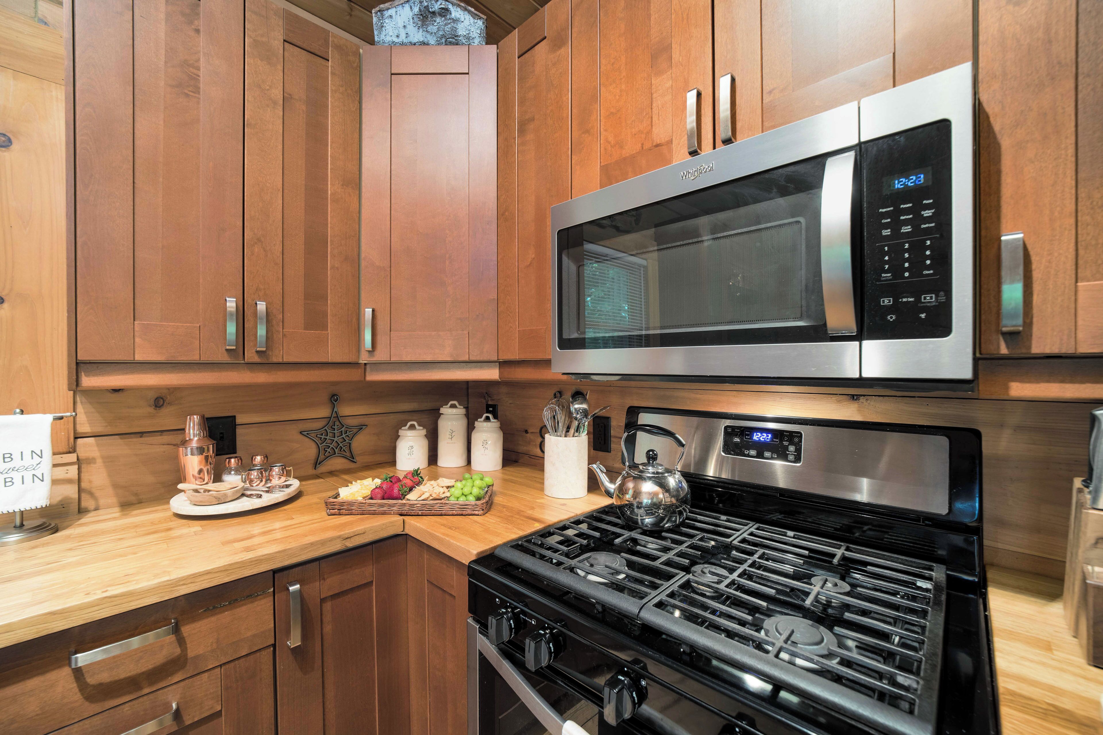 A kitchen with wooden cabinets, a stainless steel microwave, a gas stove, and various kitchen utensils.
