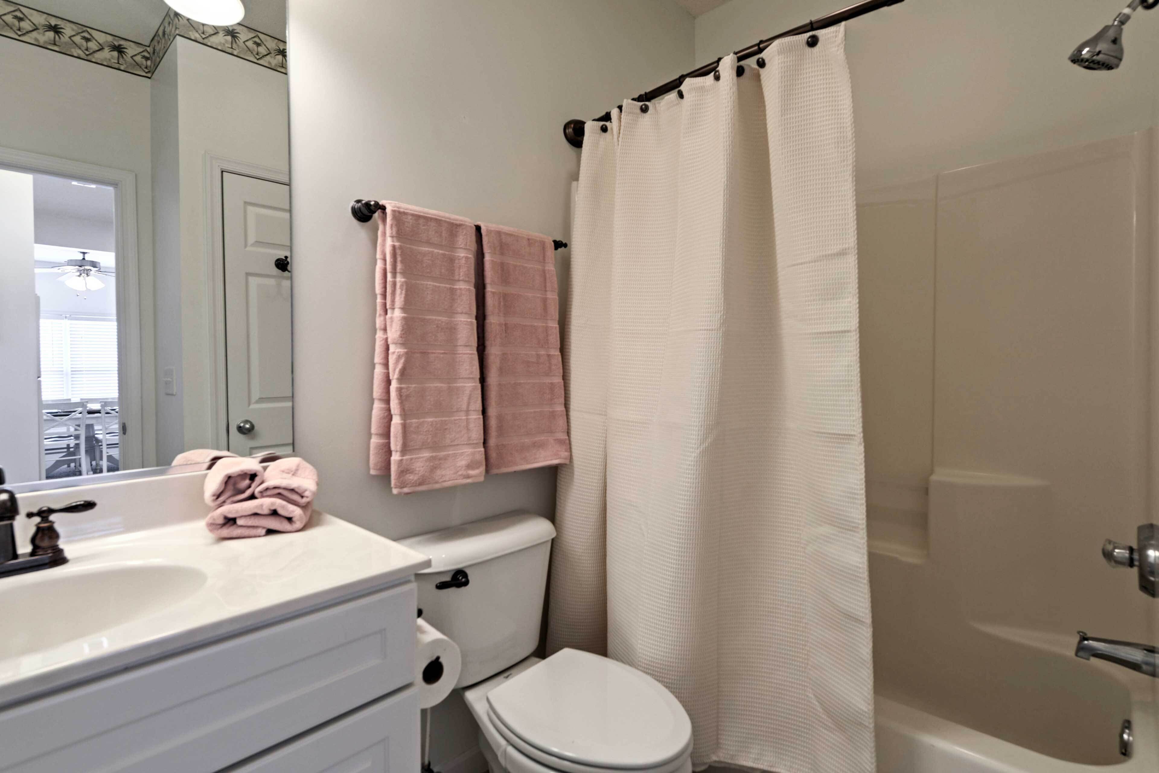 A bathroom with a white sink, toilet, and bathtub. There are pink towels hanging on the wall.
