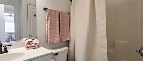 A bathroom with a white sink, toilet, and bathtub. There are pink towels hanging on the wall.
