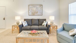 A living room with a grey sofa, two side tables with lamps, a glass coffee table, and a wall art piece. - 4 Mi to Beaches: Luxe Coastal Resort Condo (Lewes)
