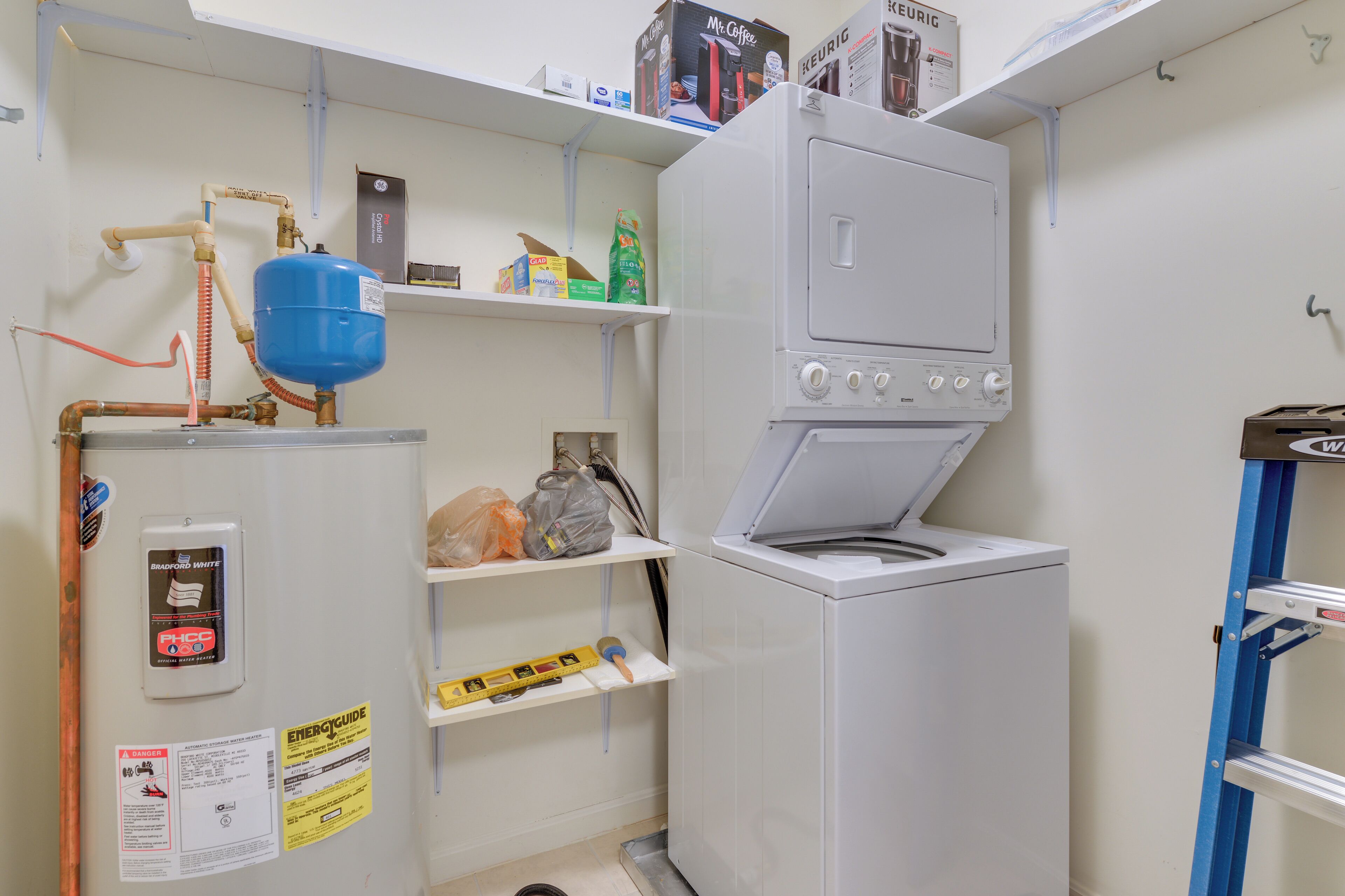 A compact laundry room with a washing machine, a water heater, and shelves with various items.
