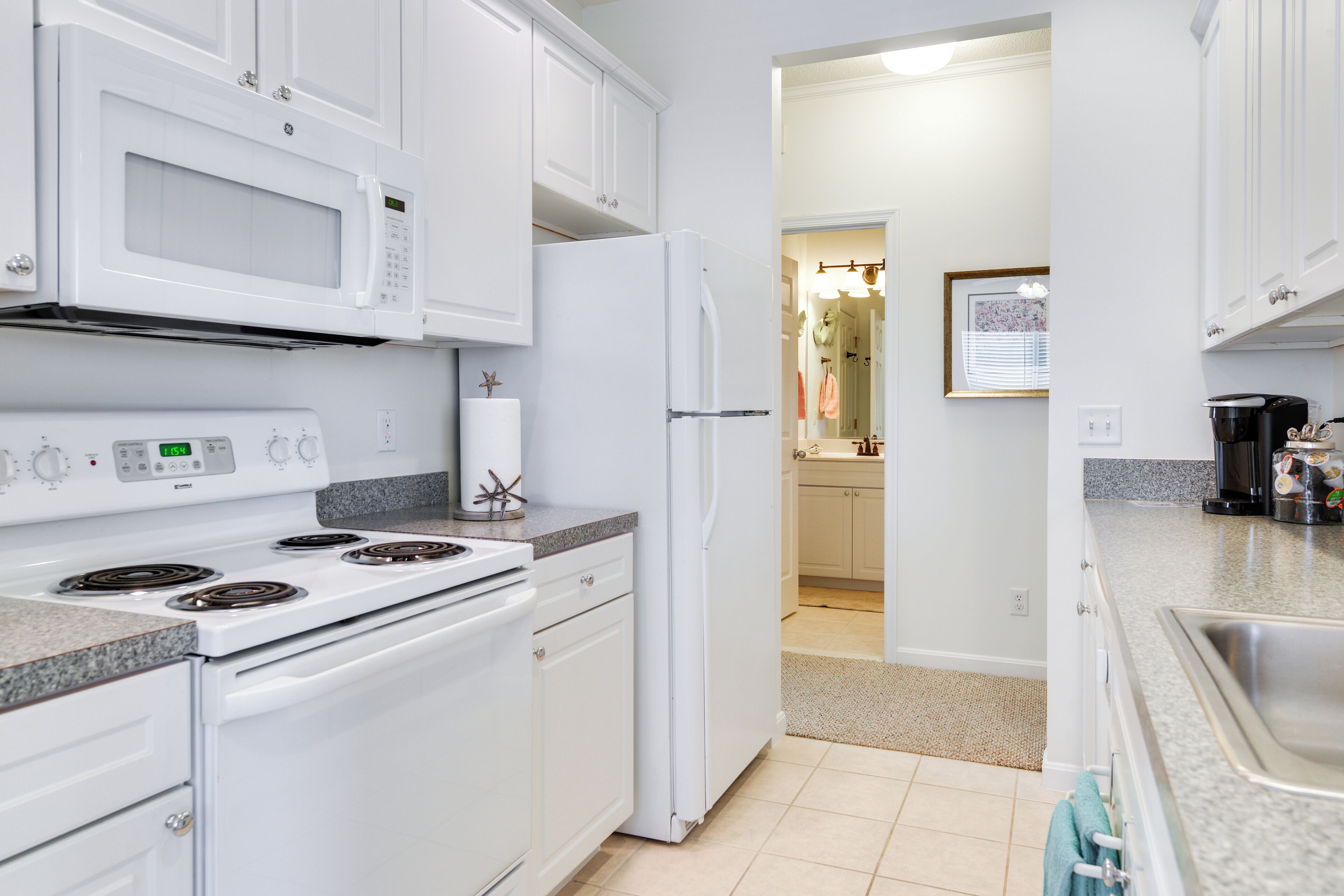 A modern kitchen with white appliances, granite countertops, and a visible hallway leading to a bathroom.