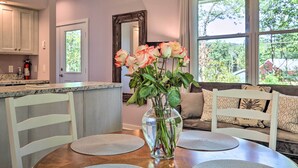 A kitchen with a dining table, chairs, a vase with flowers, and a large window with a view of greenery.