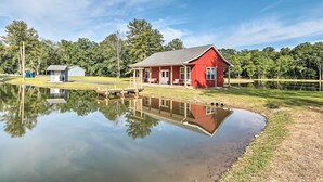 A red building with a reflection in a pond, surrounded by trees and a clear sky.