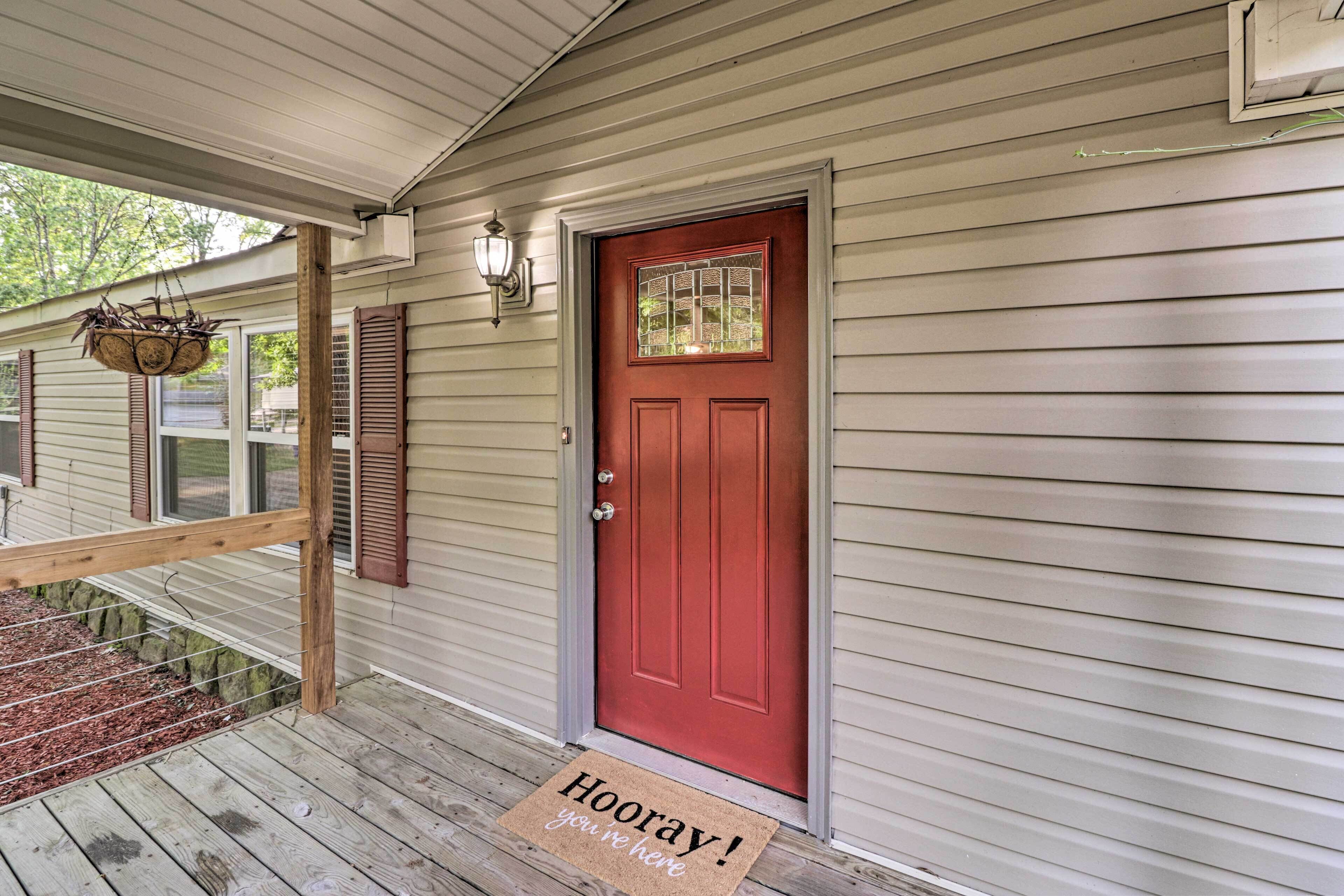 A red door with a doormat that reads "Hooray! you're here".