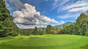 A golf course with a clear sky, lush green grass, and trees.