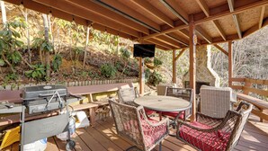 An outdoor patio with a grill, wicker furniture, and a TV mounted on the ceiling. - 1 Mile to Golfing: Porch w/ Fireplace + Mtn Views! (Maggie Valley)