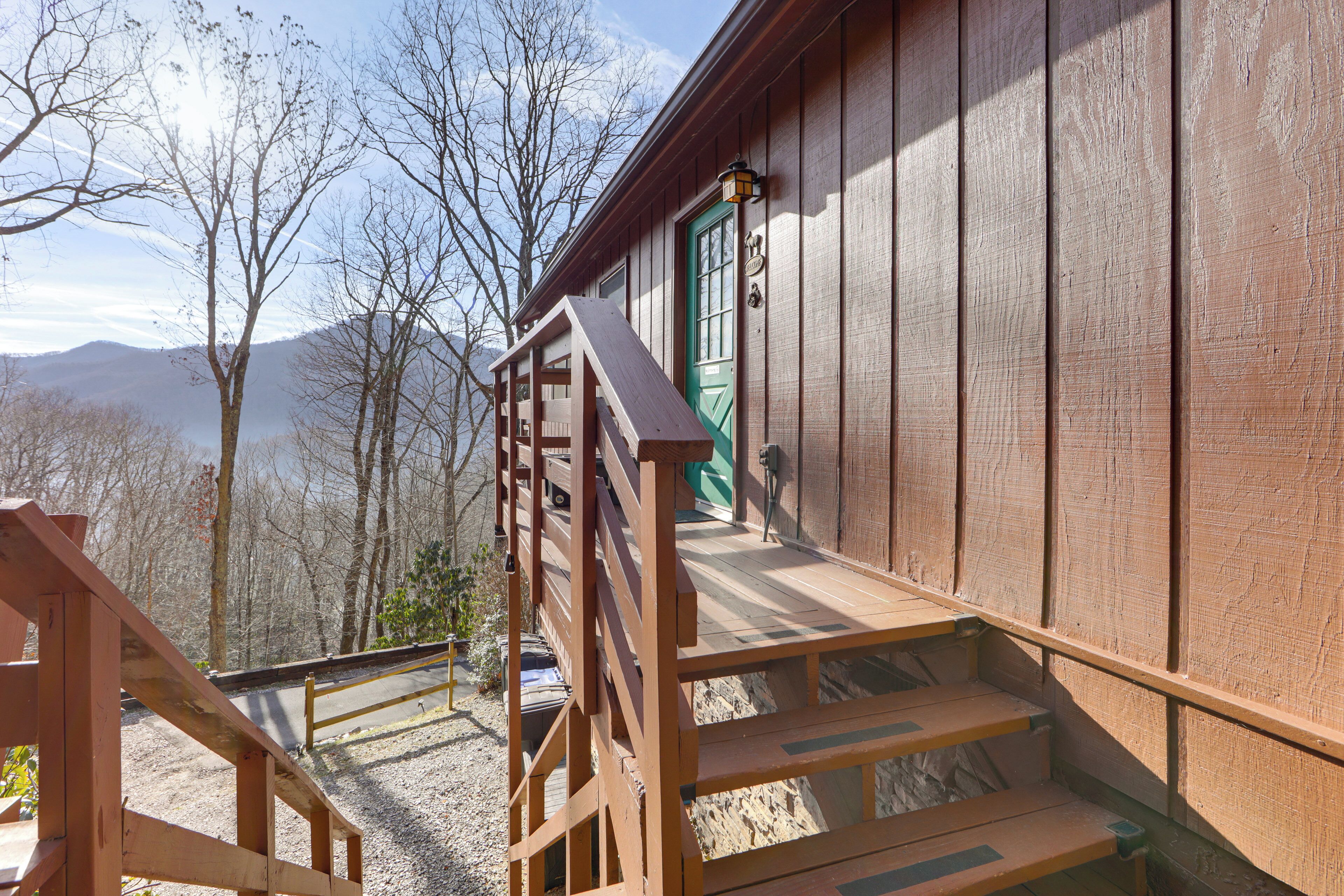 Una baita di legno con una porta verde, una scala in legno e vista sulle montagne sullo sfondo.