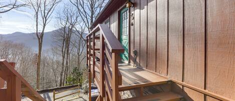 Una cabaña de madera con puerta verde, una escalera de madera y vistas a montañas al fondo.
