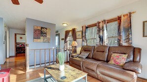 A spacious living room with a brown leather sofa, a wooden coffee table, and a view of the outdoors through large windows.
