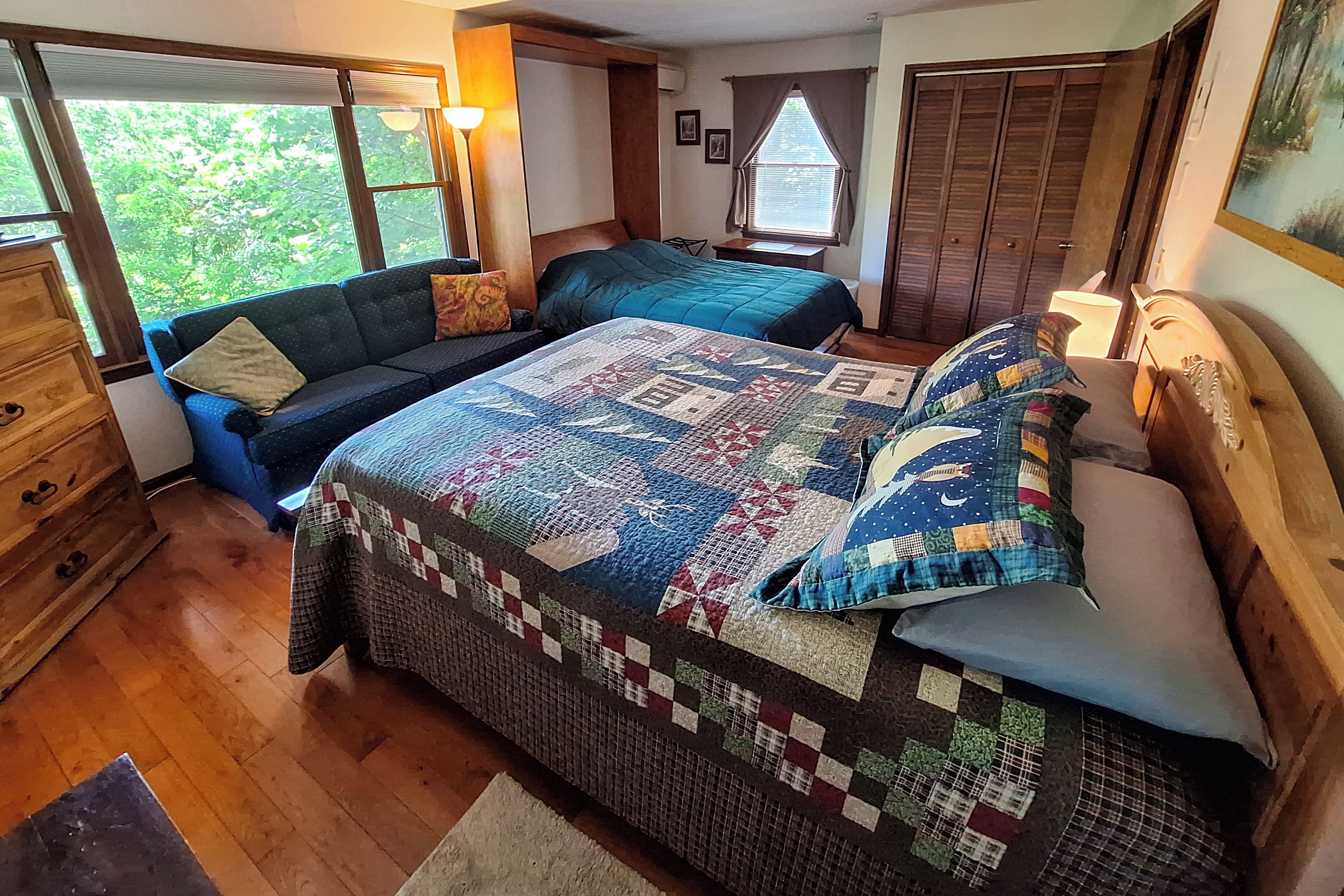 A bedroom with a large bed, a sofa, a dresser, and a window with curtains.