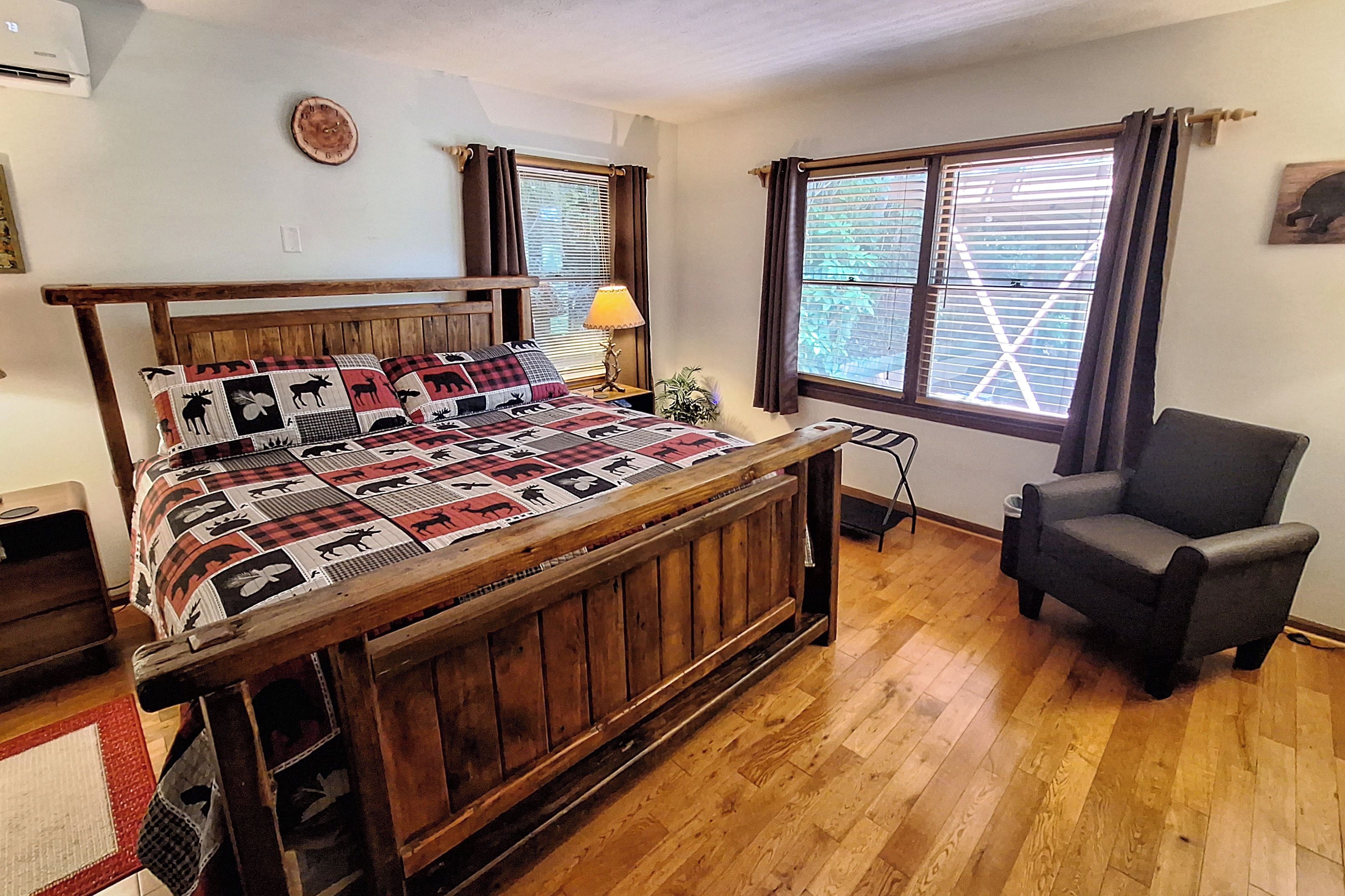 A bedroom with a wooden bed, a chair, a window with blinds, and a wall clock.