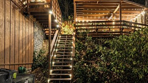 A wooden staircase with railings, a wooden deck, and a garden area with bushes.