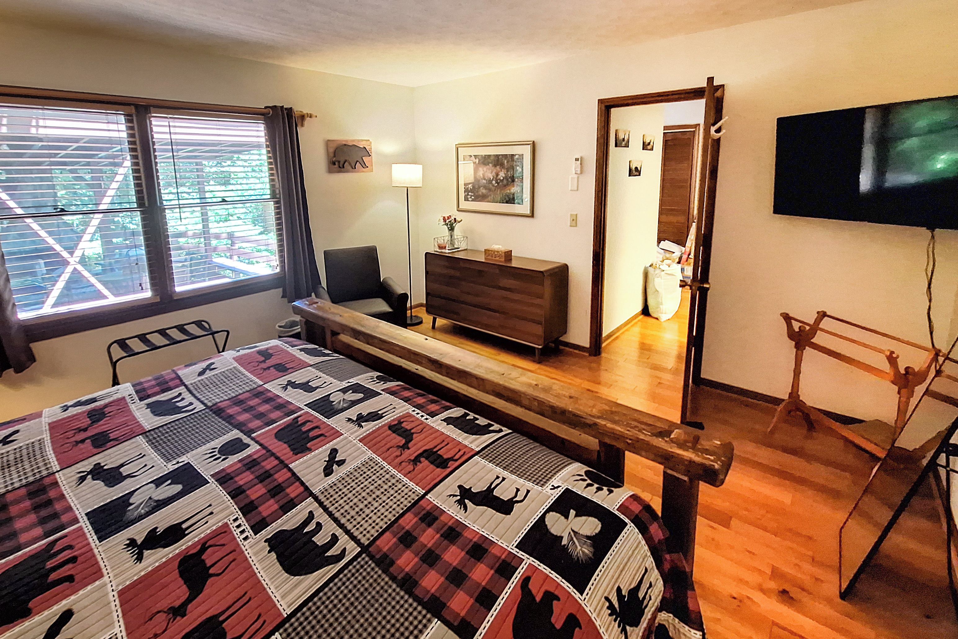 A bedroom with a bed, a dresser, a chair, a desk, a TV, and a window with blinds.