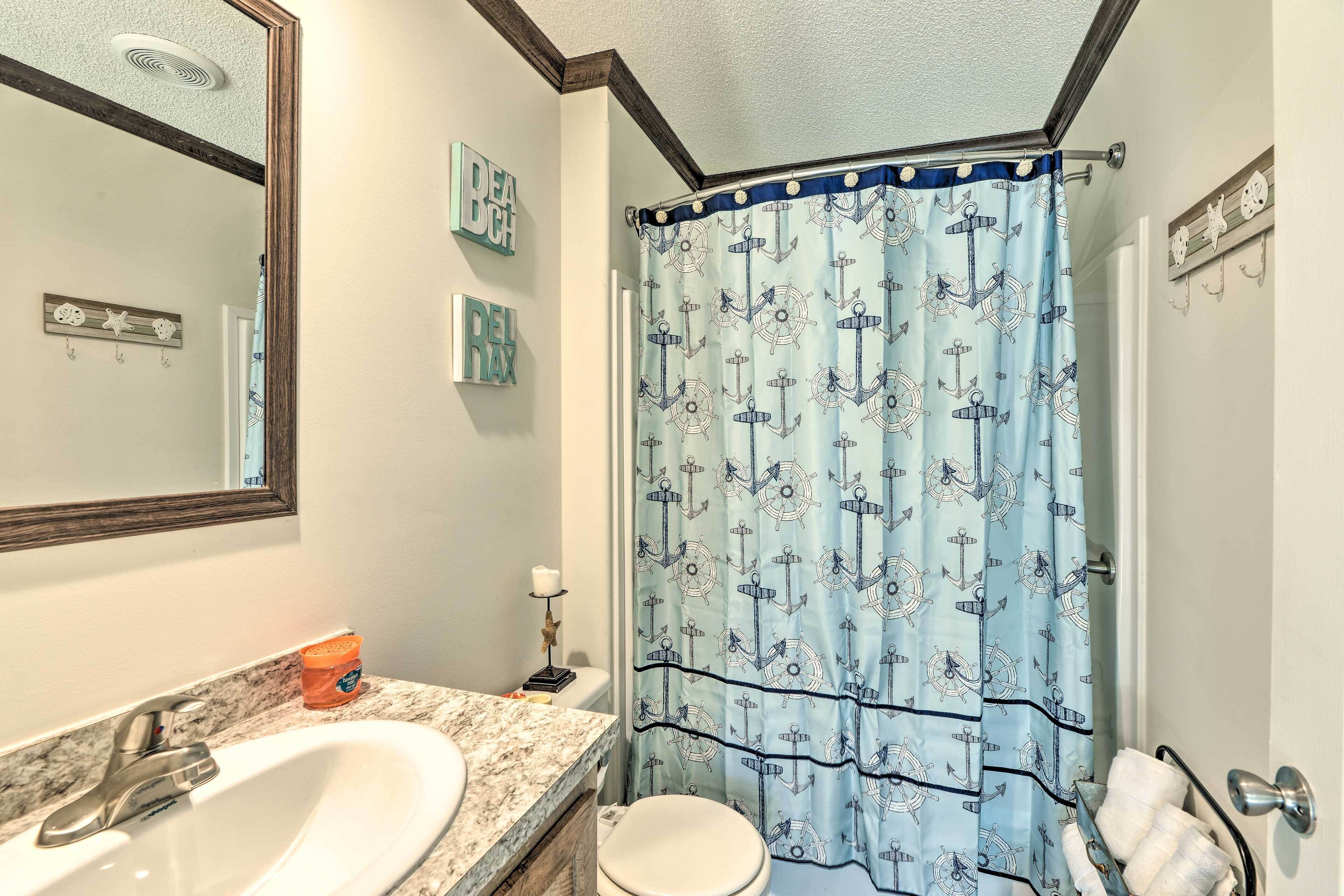 A bathroom with a white sink, a toilet, and a shower curtain with an anchor pattern.