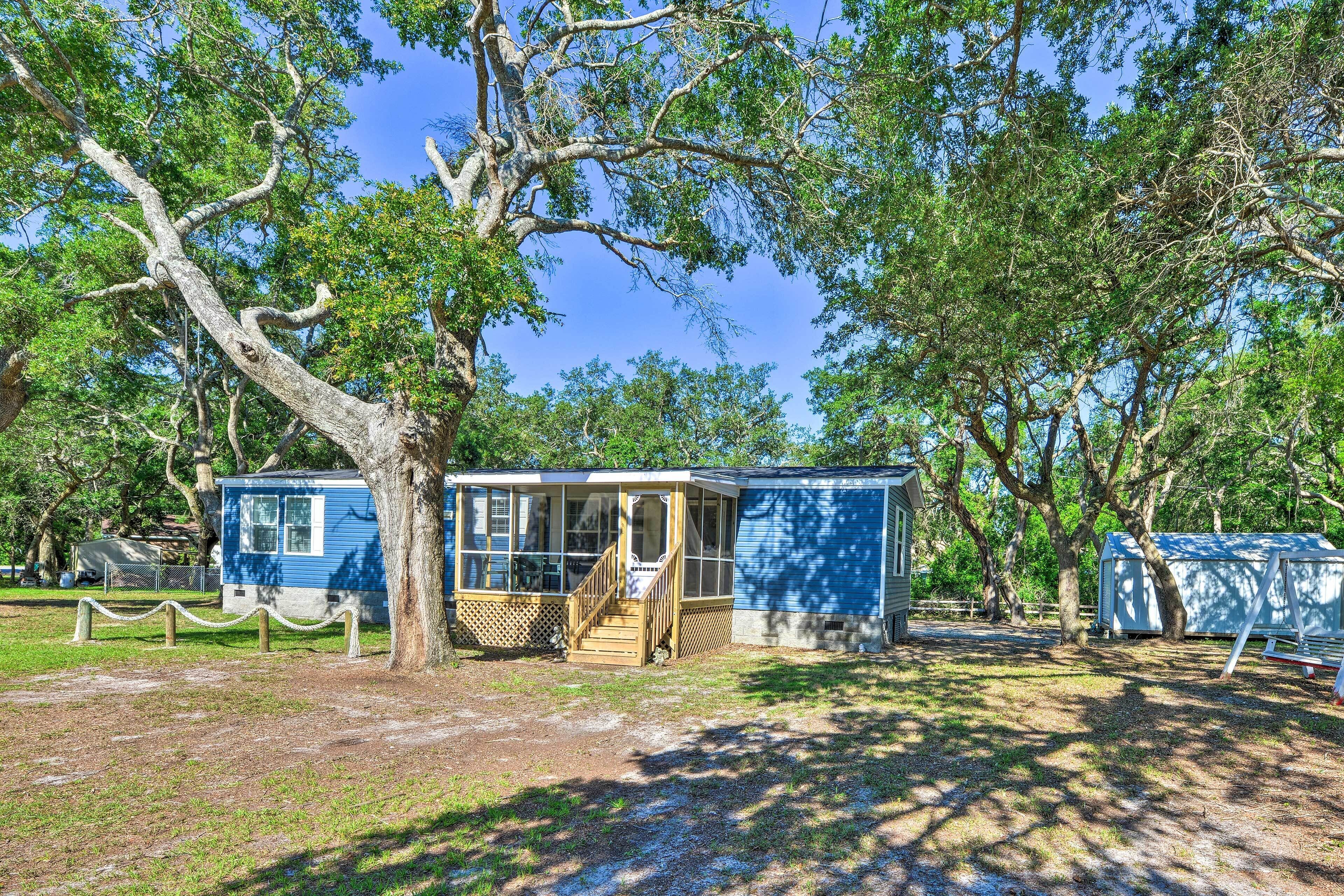 A small, single-story cabin with a porch, surrounded by trees.