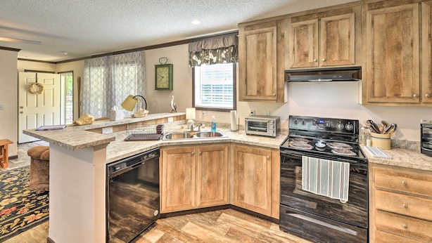 A kitchen with wooden cabinets, a built-in dishwasher, a stove, and a window with a view. - 'pelican Place' Coastal Cottage Walk to Back Sound (Harkers Island)