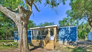 A small, single-story building with a porch and a covered area, surrounded by trees and a clear sky. - 'pelican Place' Coastal Cottage Walk to Back Sound (Harkers Island)
