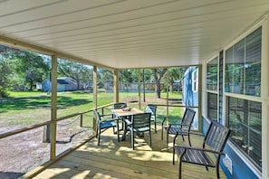 Un patio cubierto con una mesa y sillas, con vista a un jardín con césped y una casa.