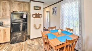 A compact kitchen with wooden cabinets, a black refrigerator, and a dining area with a wooden table and blue placemats. - 'pelican Place' Coastal Cottage Walk to Back Sound (Harkers Island)
