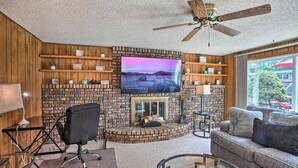 A living room with a brick fireplace, a television mounted on the wall, and a ceiling fan. - Spacious Family Glenwood Estates Home w/ Hot Tub! (Glenwood)