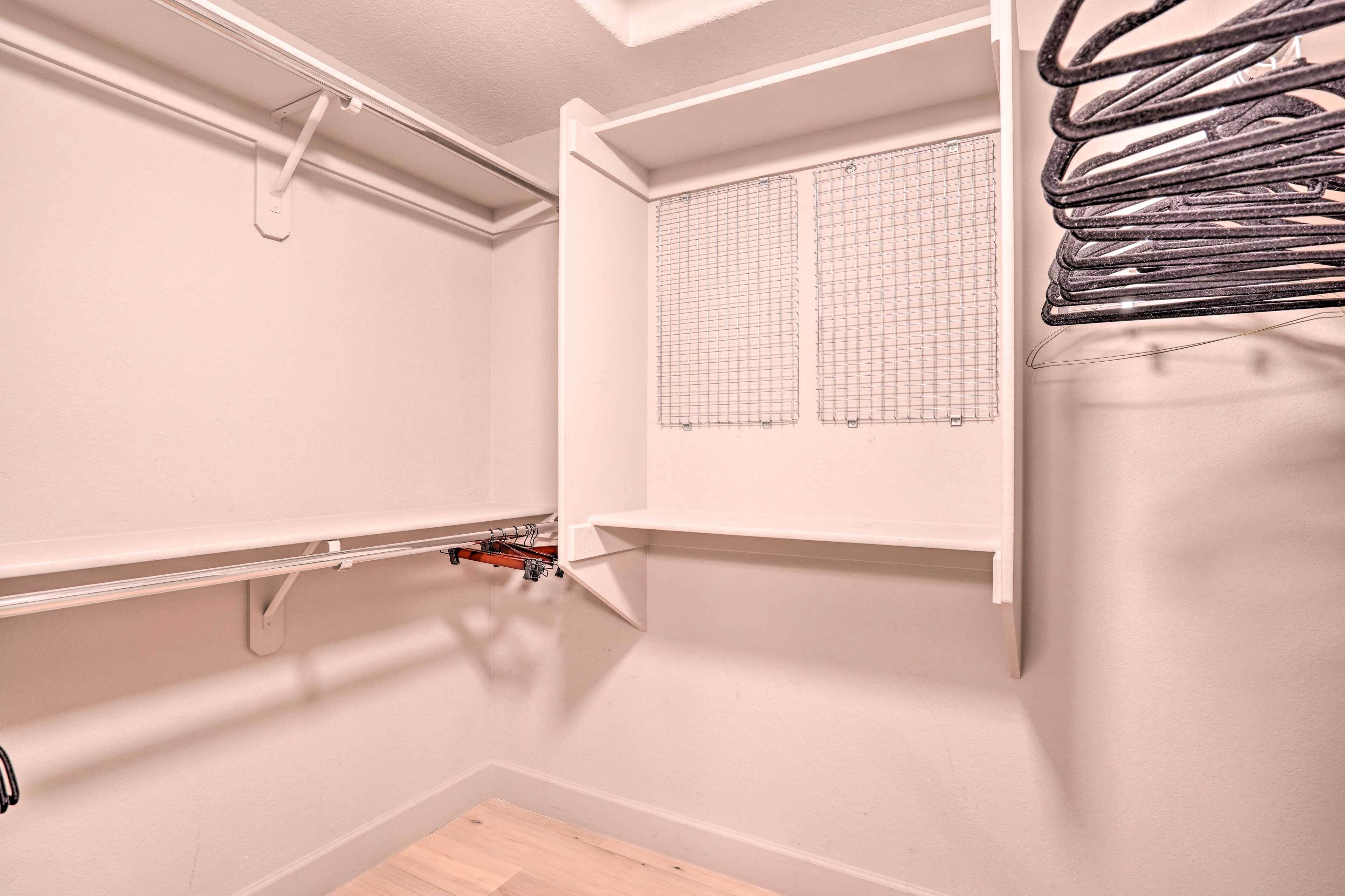 Una esquina de una habitación con pared blanca, una ventana con persianas de celosía y una estantería metálica con objetos.