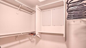 Un coin de pièce avec un mur blanc, une fenêtre avec des stores à lamelles et un étagère métallique sur laquelle sont posés divers objets.