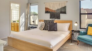 A modern bedroom with a large bed, a bedside table with a lamp, a chair, and a view of the outside. - Pet-friendly Snowbird Haven w/ Pool in Gold Canyon (Gold Canyon)
