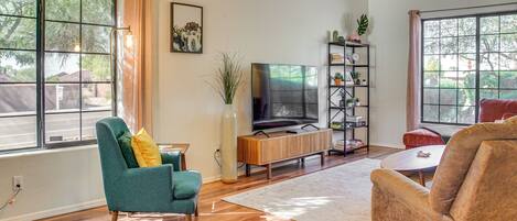 A living room with wooden flooring, a television, a bookshelf, and a large window.
