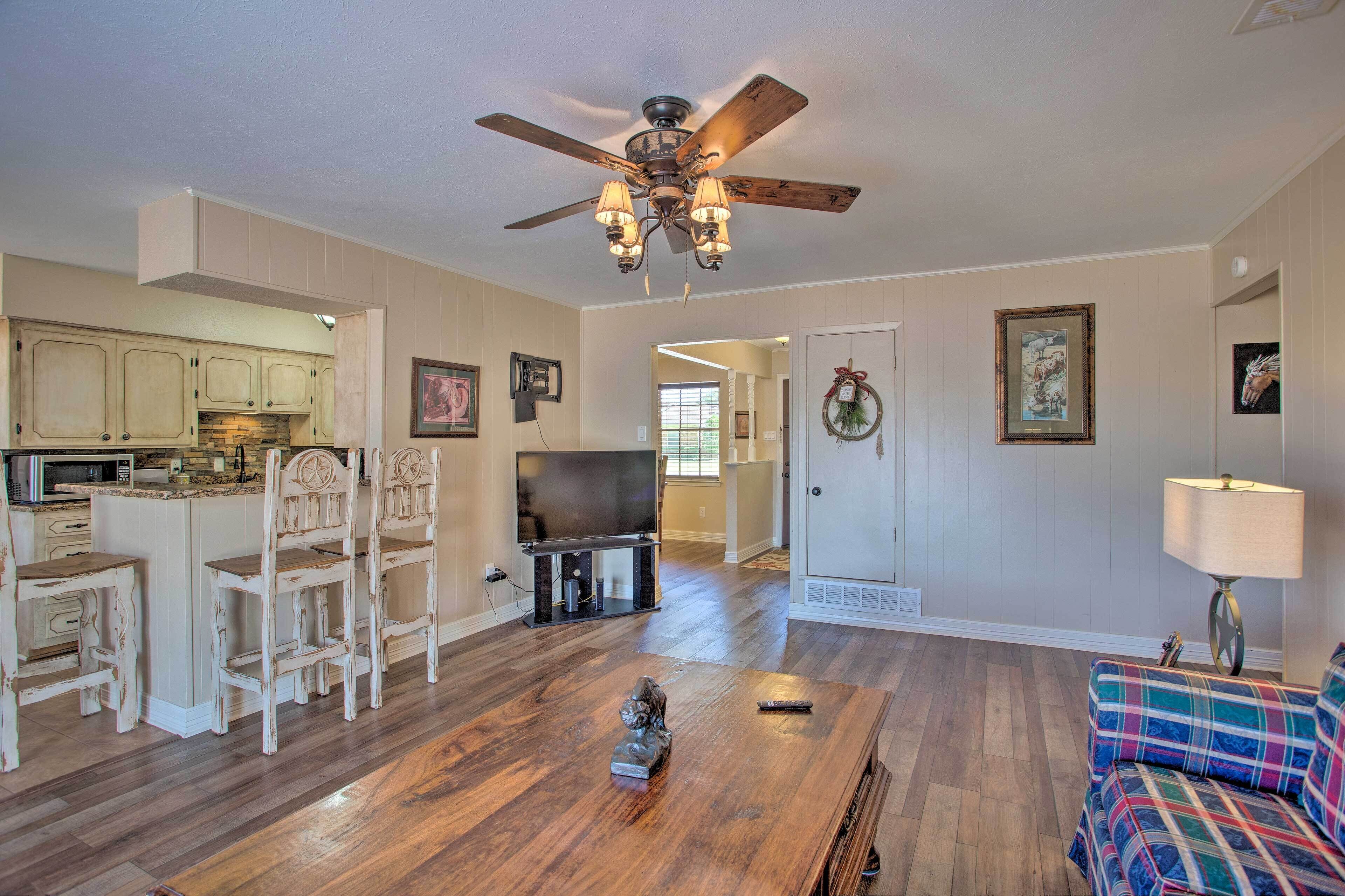 A spacious living room with a wooden floor, a ceiling fan, a television, and a sofa.