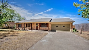 A single-story house with a garage, brick exterior, and a front yard with sparse grass. - Home in Historic Waxahachie w/ Yard & Patio! (Waxahachie)