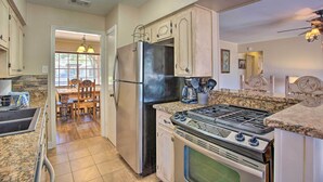 A kitchen with a refrigerator, stove, oven, granite countertops, and a dining area with a table and chairs. - Home in Historic Waxahachie w/ Yard & Patio! (Waxahachie)