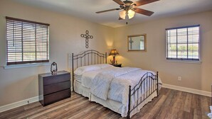 A bedroom with a bed, a dresser, a ceiling fan, and two windows with blinds. - Home in Historic Waxahachie w/ Yard & Patio! (Waxahachie)