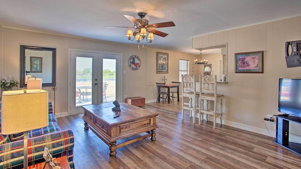 A spacious living room with a wooden floor, a ceiling fan, a television, and a dining area with chairs and a table. - Home in Historic Waxahachie w/ Yard & Patio! (Waxahachie)