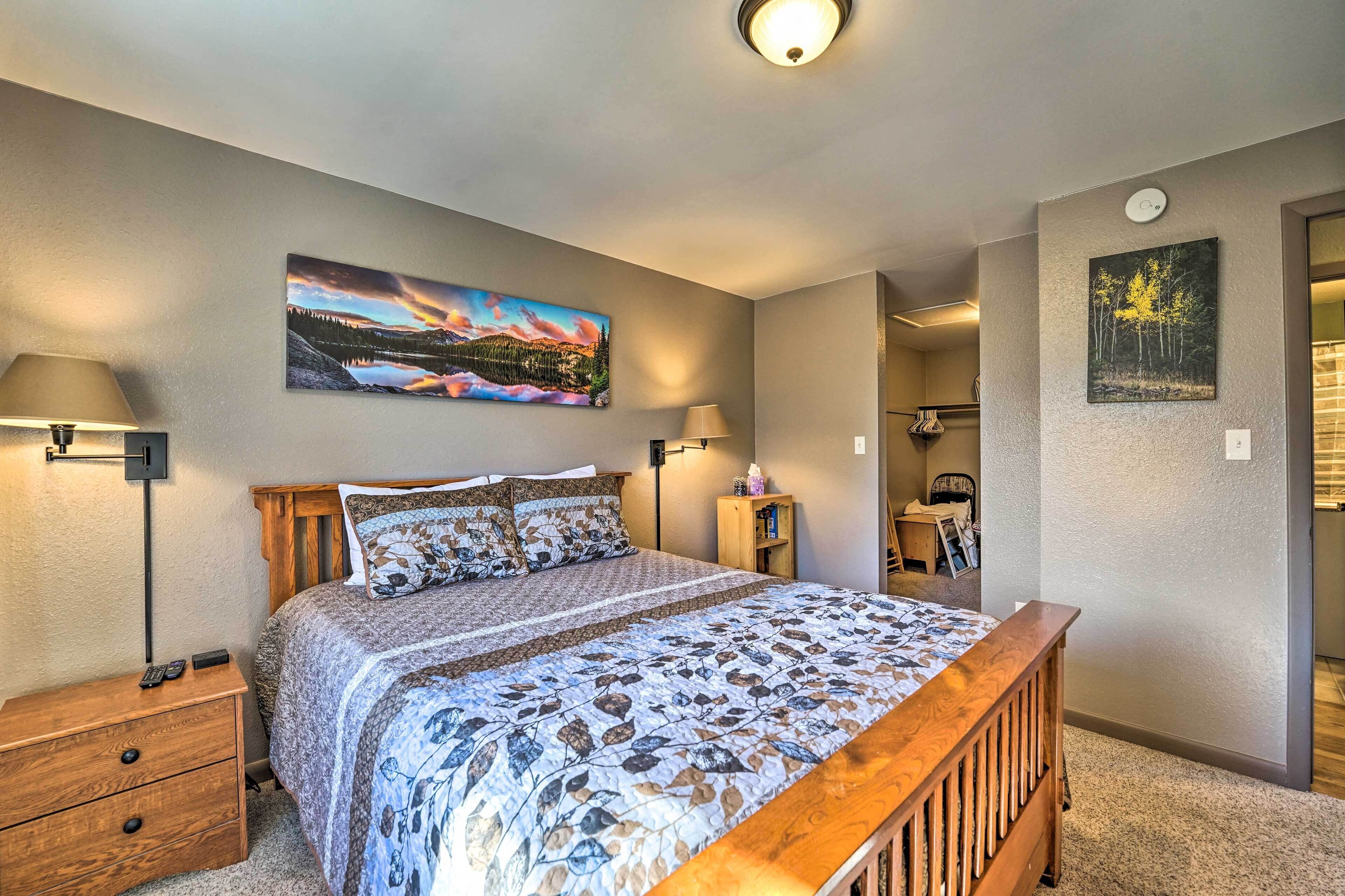 A bedroom with a wooden bed, two bedside tables, a nightstand, and a wall-mounted lamp.
