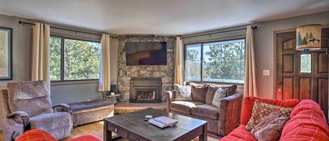 A cozy living room with a stone fireplace, comfortable seating, and large windows.