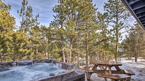 A hot tub surrounded by a wooden picnic table and benches, set against a backdrop of pine trees and a snowy ground. - Luxe Updated Home w/ Grill + Hot Tub: 4 Mi to Rmnp (Estes Park)