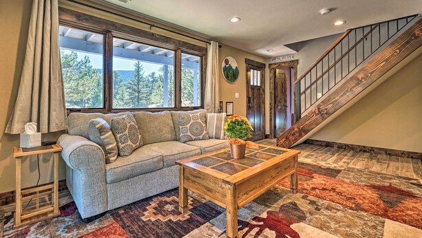 A living room with a sofa, a coffee table, and a staircase. - Luxe Updated Home w/ Grill + Hot Tub: 4 Mi to Rmnp (Estes Park)